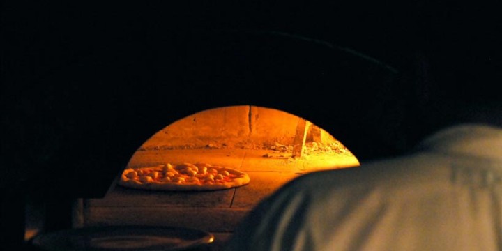 Dark, glowing brick oven interior with a pizza inside, warm orange and yellow light