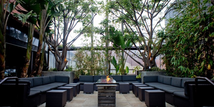 Layered paper-cut collage of an outdoor patio with dark sofas, a central fire pit, and surrounding greenery